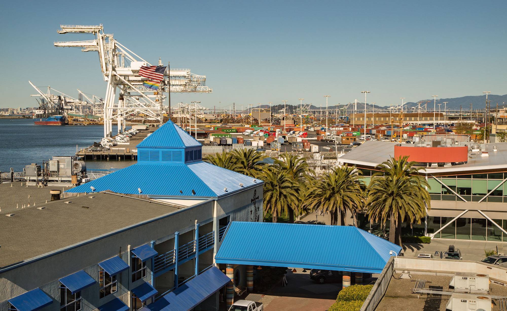 Horizontal photo of the Waterfront hotel and the waterfront. There are flags, bright blue roofs and large pieces of equipment visible